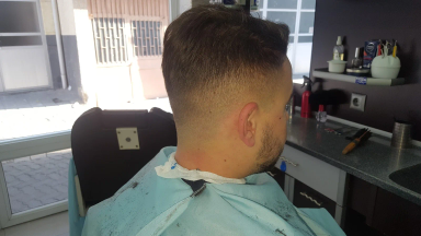 Prerje fade e klientit në karrigen e berberit me pelerinë